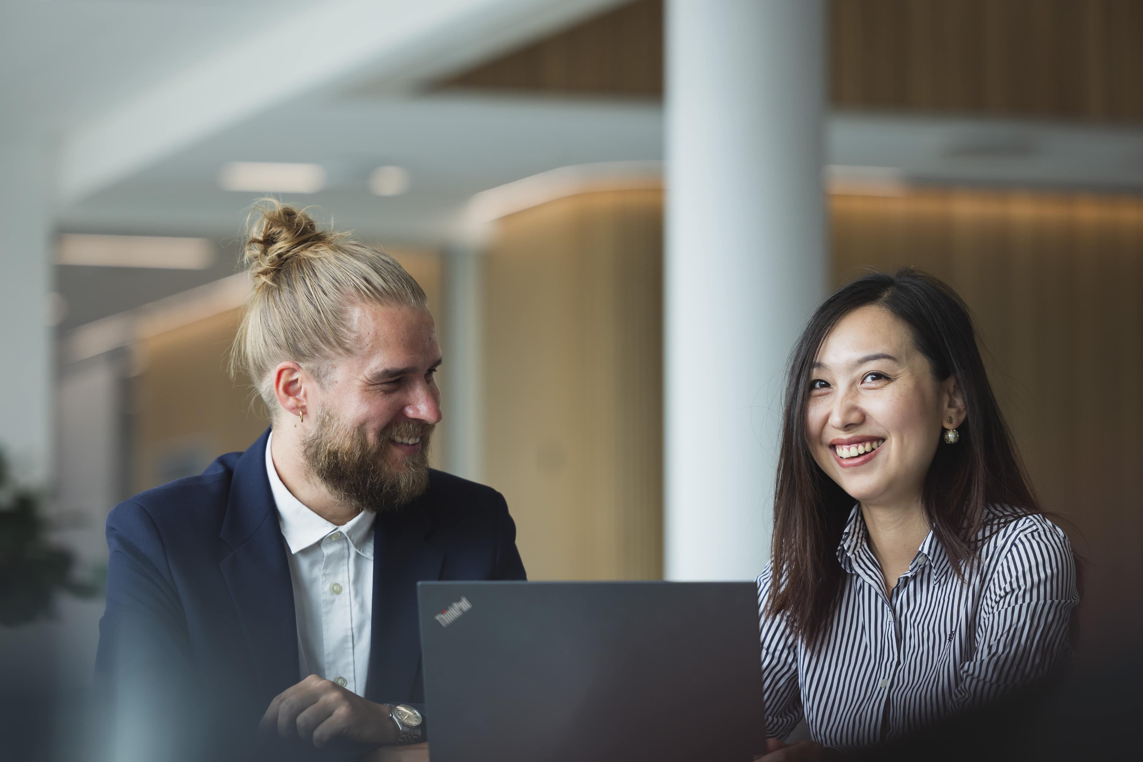 Two office workers, smiling, sitting at a table with a laptop in front of them