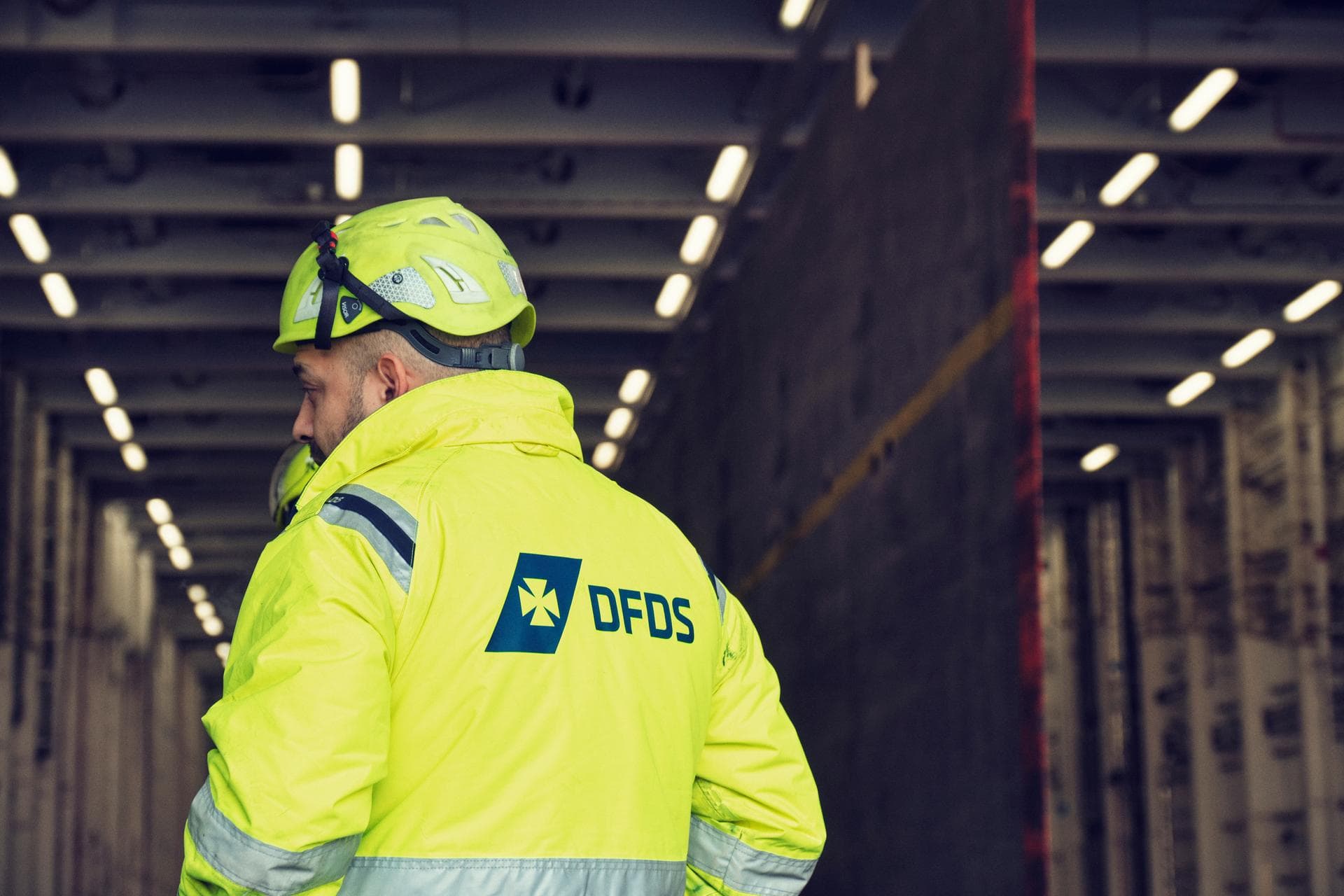 DFDS worker with a yellow helmet & DFDS security jacket, in the hull of a vessel, working