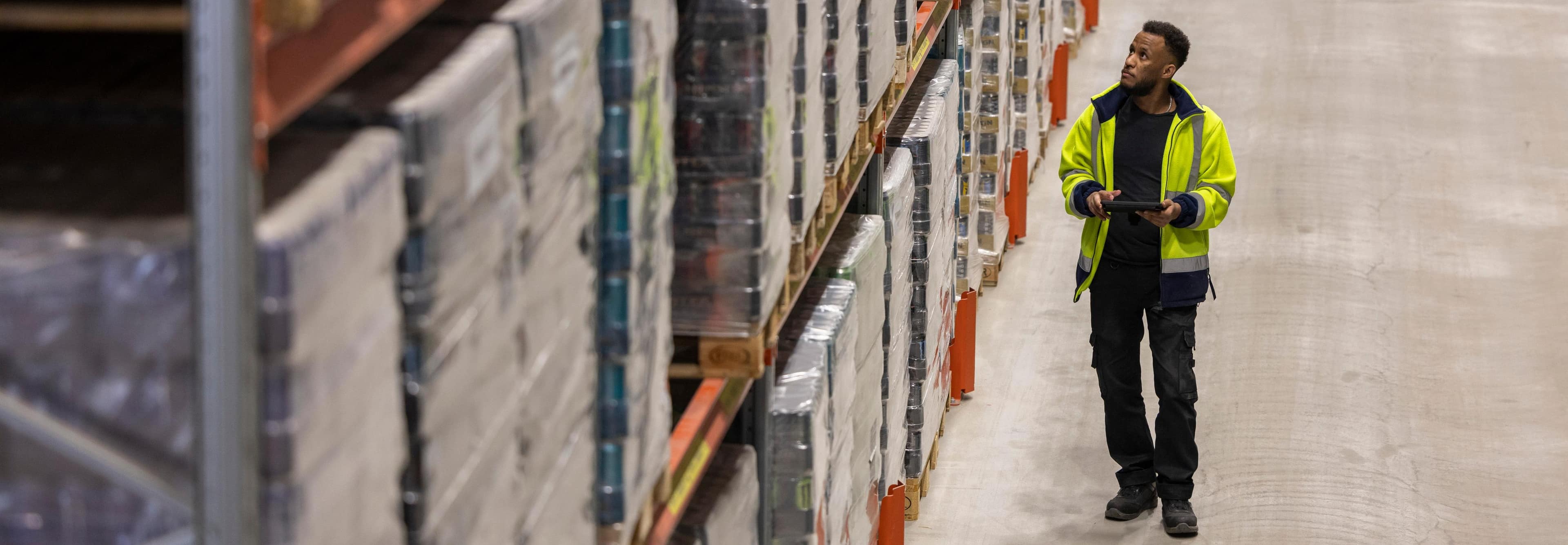 A DFDS employee wearing a high visibility jacket walks past a stack of pallets at a warehouse