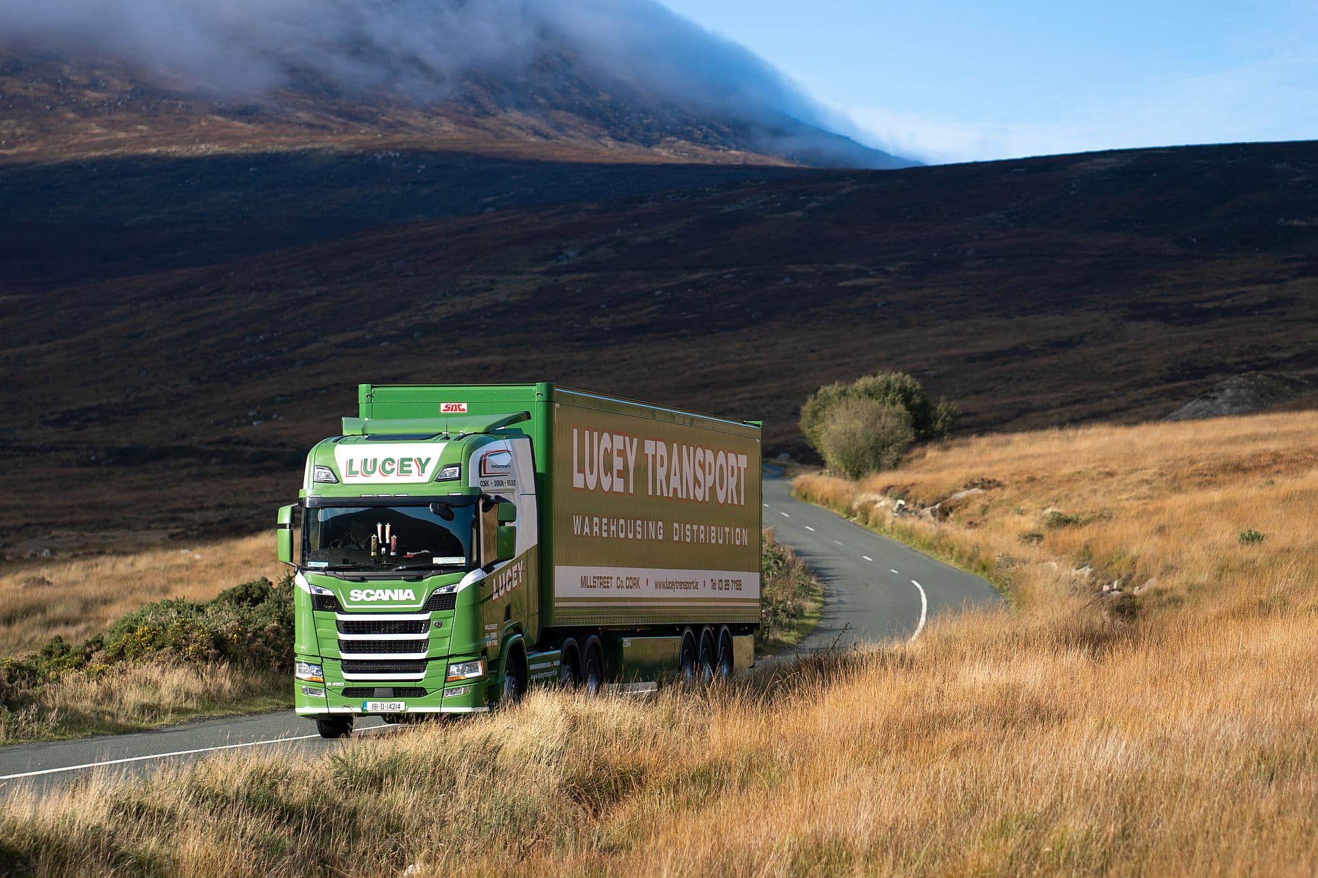 Truck of Lucey Transport Logistics Ltd. driving on the road in a natural and hilly environment