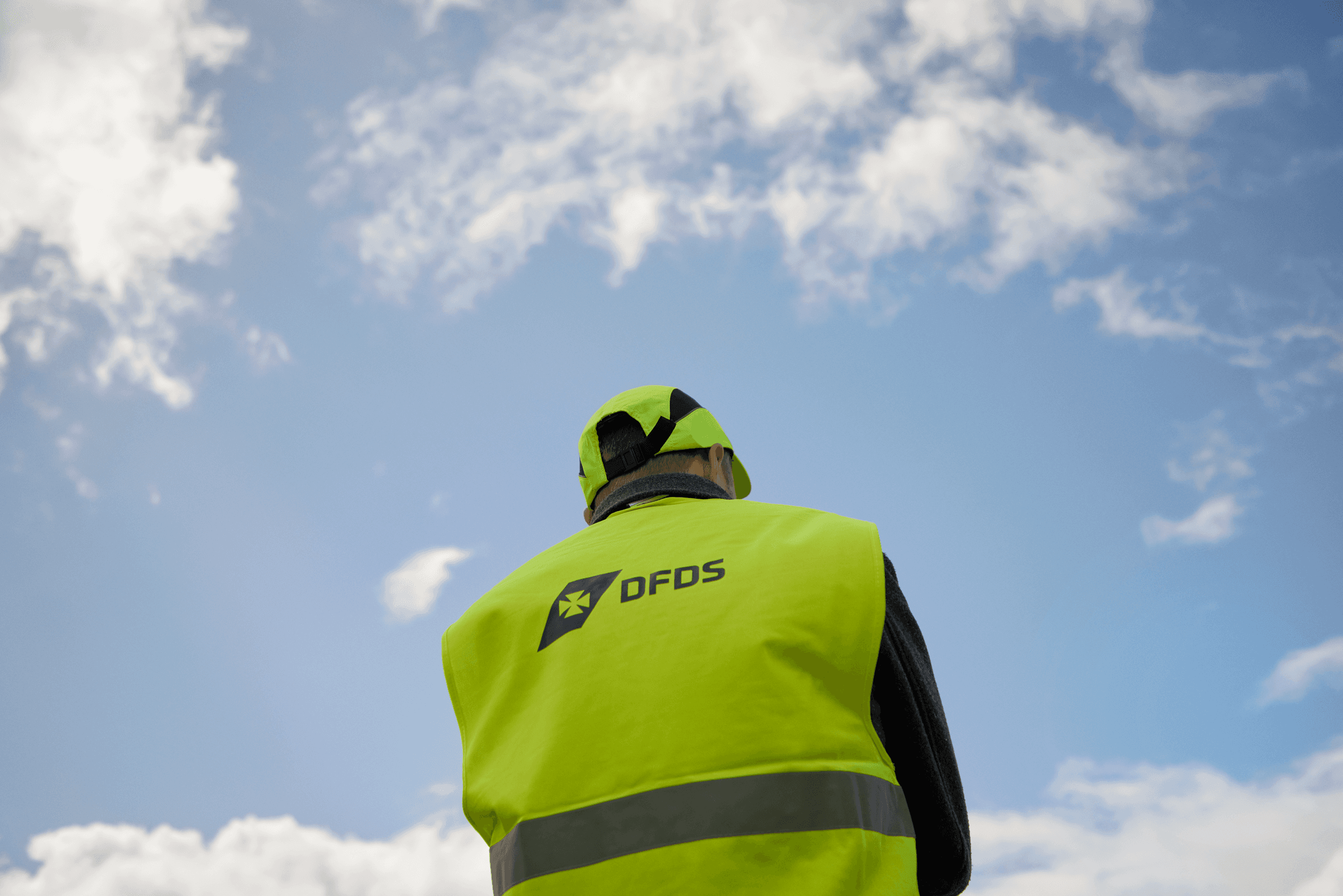 DFDS worker wearing a safety vest, with clouds in the background.