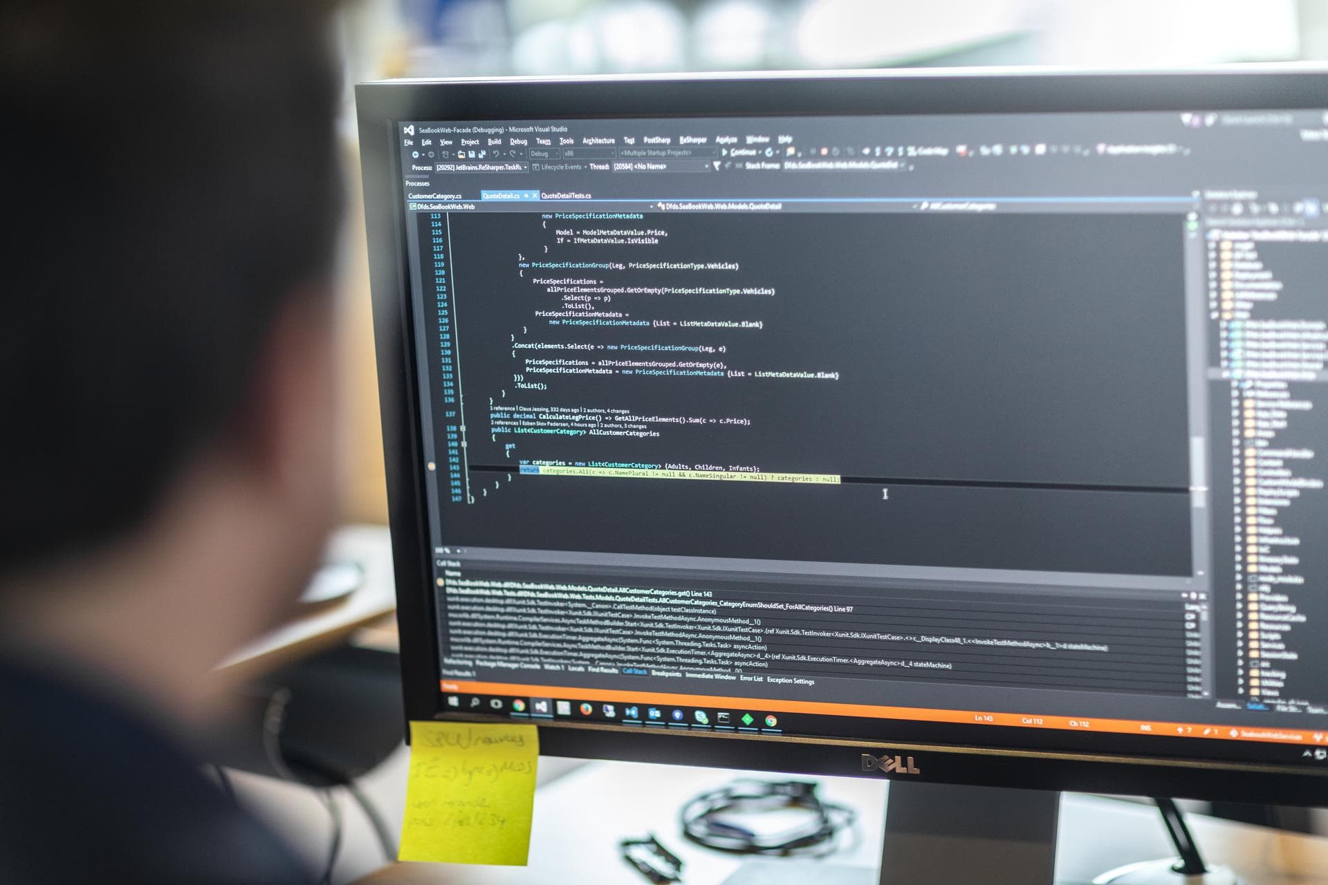 A person sitting in front of a PC monitor, screen showing code on dark background